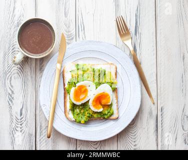 Sandwich aux œufs d'avocat avec une tasse de cacao chaud. Concept de petit déjeuner léger et sain. Toasts de grains entiers avec de la purée d'avocat et des œufs frits et des graines de citrouille Banque D'Images