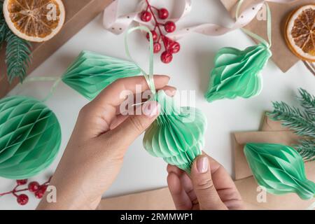 Les mains féminines déplient des ornements en nid d'abeille de Noël en papier. Décoration sans plastique pliable faite à la main. Concept d'artisanat de créativité hivernale. Mode éco DIY. SC Banque D'Images