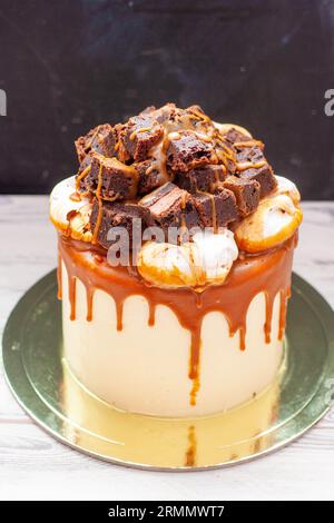 Délicieux gâteau à la vanille avec morceaux de brownie hachés, nuages de meringue et sauce caramel salé fondu Banque D'Images