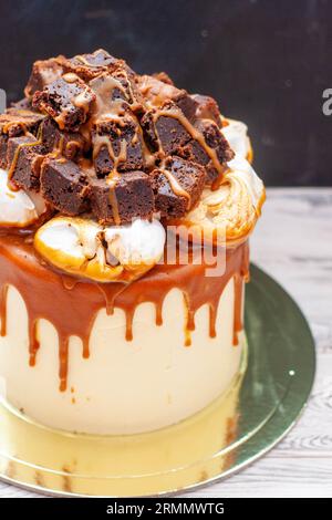 Délicieux gâteau à la vanille avec morceaux de brownie hachés, nuages de meringue et sauce caramel salé fondu Banque D'Images