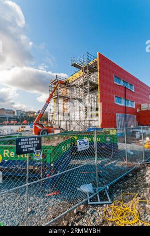 Un grand ascenseur de location orange avec son bras étendu au toit d'un bâtiment sur un chantier de construction. Il est utilisé pour transporter les matériaux de construction jusqu'au toit. Banque D'Images