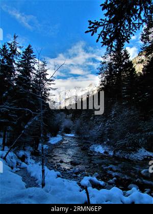 Rivière coulant à travers la vallée de Vrata en hiver dans le parc national de Triglav et alpes Juliennes à Gorenjska Slovénie en hiver et le soleil illuminé sommets des montagnes S Banque D'Images