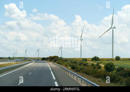 Les éoliennes se dressent le long de la route sur fond de nuages. Production d'énergie écologique verte. Banque D'Images