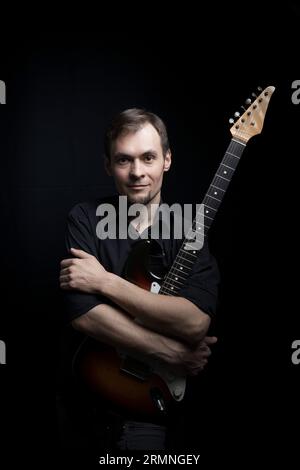 Portrait calme d'un gars avec une guitare électrique sur fond noir Banque D'Images