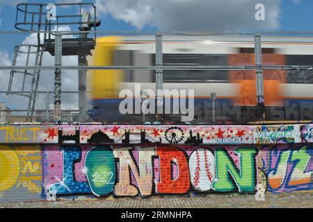 Le mot London est écrit en lettres graffiti à côté d'un train londonien passant à Shoreditch East London Banque D'Images