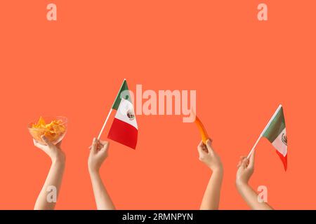 Mains féminines tenant nachos, piment et drapeaux mexicains sur fond orange Banque D'Images