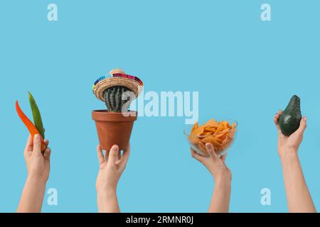 Mains femelles tenant avocat, nachos, cactus et piments forts sur fond bleu Banque D'Images