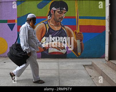 Un homme musulman portant un sac passe devant une peinture murale représentant l'athlète indien Neeraj Chopra à Mumbai. Neeraj Chopra est devenu le premier Indien à remporter la médaille d'or au Championnat du monde d'athlétisme organisé à Budapest en Hongrie. Il a réussi à lancer le javelot à une distance de 88.17m qui lui a valu la médaille d'or devant le pakistanais Arshad Nadeem qui a remporté une médaille d'argent. Banque D'Images