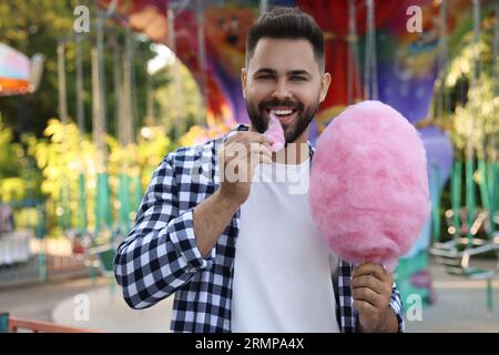 Heureux jeune homme mangeant des bonbons de coton au funfair Banque D'Images