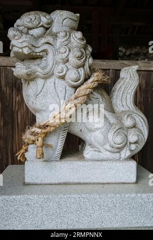 Japon, Kyushu. Gardien de chien-lion au temple bouddhiste Tennen-ji et au sanctuaire shinto. La corde shimenawa indique un espace sacré ou rituellement pur. Banque D'Images