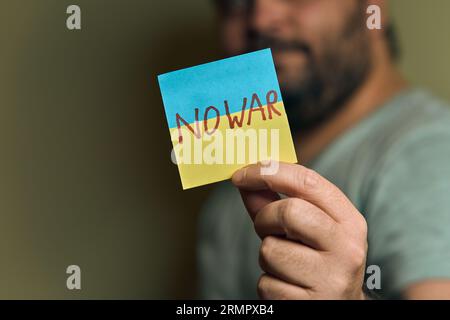 Un européen barbu tient un autocollant devant lui, sous la forme d'un drapeau ukrainien avec l'inscription no war Banque D'Images