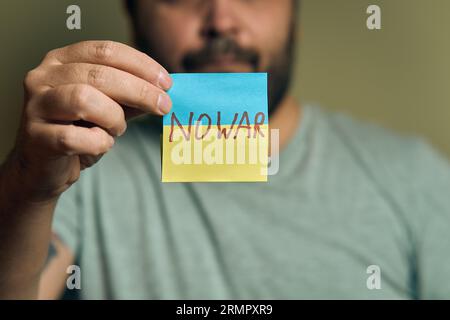 Un européen barbu tient un autocollant devant lui, sous la forme d'un drapeau ukrainien avec l'inscription no war Banque D'Images