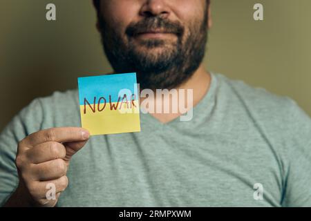 Un européen barbu tient un autocollant devant lui, sous la forme d'un drapeau ukrainien avec l'inscription no war Banque D'Images