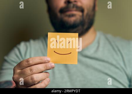 Un européen barbu tient un autocollant orange devant lui, avec un visage souriant Banque D'Images