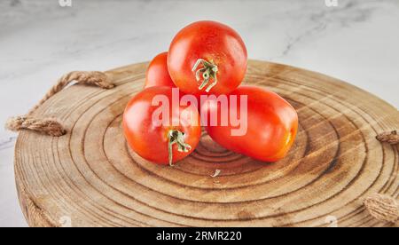 Tomates prune empilées dans la colline sur un fond en bois sur marbre blanc Banque D'Images