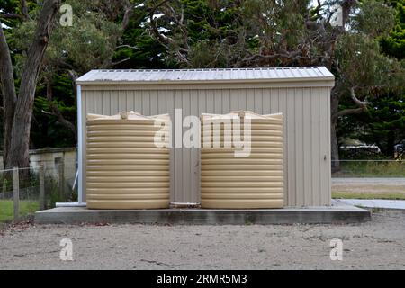 Deux réservoirs d'eau en plastique sur une base en béton à l'extérieur sont la caractéristique de durabilité d'un petit hangar agricole sur une propriété australienne avec un fond de gommier Banque D'Images