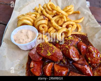 Currywurst allemand traditionnel, servi avec des frites sur Une assiette blanche.Table en bois comme arrière-plan. Banque D'Images