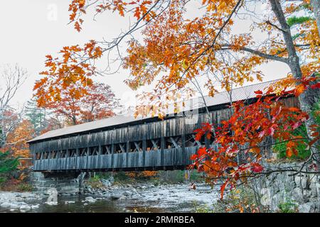 Pont historique d'Albany sur la rivière Swift, près de North Conway, NH avec de beaux arbres d'automne et des feuilles et quelques rochers montrant dans la rivière peu profonde. Banque D'Images
