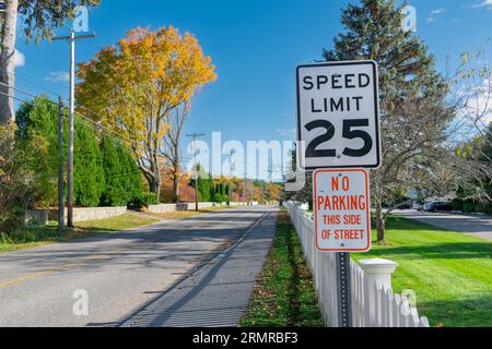 Limite de vitesse américaine traditionnelle et pas de panneaux de stationnement au-dessus d'une clôture de piquet blanche sur Ocean Ave, Kennebunkport, Maine USA, bordée d'arbres dorés de chute. Banque D'Images