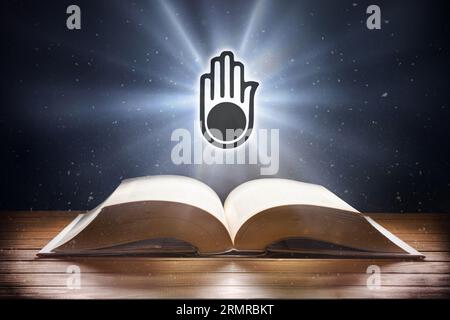 Open book on wooden table and Jainism symbol with beam of light with dark background. Front view. Stock Photo