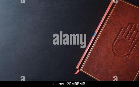 Livre de culture et de religion jaïn avec symbole religieux gravé sur la couverture en cuir brun sur une table noire. Vue de dessus. Banque D'Images