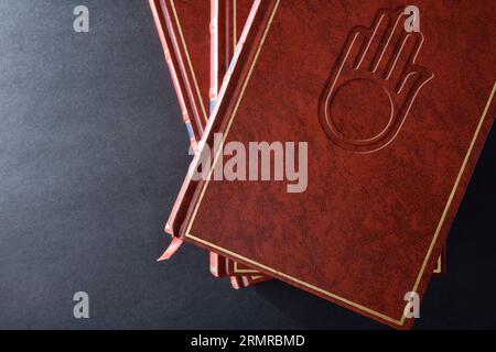 Pile de livres avec couverture en cuir brun avec symbole gravé de la culture et de la religion jaïnes sur la table noire. Vue de dessus. Banque D'Images