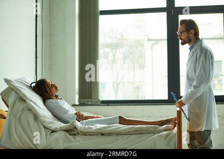 médecin debout avec presse-papiers près de femme afro-américaine, salle privée, hôpital, consultation Banque D'Images
