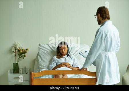 médecin debout avec presse-papiers près de femme afro-américaine, salle privée, hôpital, consultation Banque D'Images