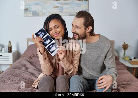 heureux mari et femme interracial, futurs parents, femme enceinte tenant l'échographie Banque D'Images