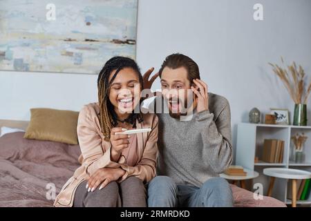 joyeux couple interracial tenant le test de grossesse, futurs parents, femme et homme afro-américains Banque D'Images