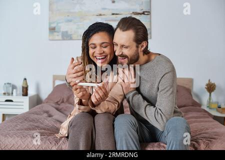 couple interracial tenant des vêtements de bébé mignons, chaussures minuscules, futurs parents, femme africaine enceinte Banque D'Images