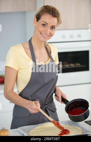 femme faisant de la pizza mettant de la sauce tomates Banque D'Images