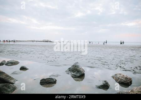 Rocks on the puddle of the beach while low tide with many people in the background Stock Photo