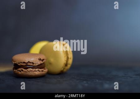 Macarons of brown and yellow tones drop on a slate plate on a black background. Stock Photo