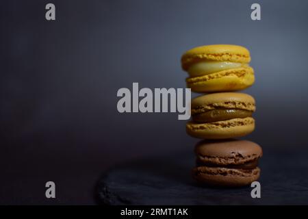 Tour de macarons bruns et jaunes sur plaque d'ardoise avec fond noir éclairé Banque D'Images