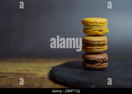 Macarons brun et jaune teintés empilés sur plaque d'ardoise et fond noir. Banque D'Images