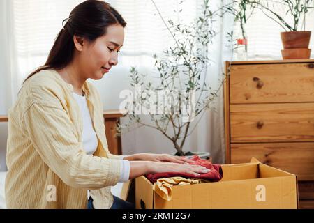 femme asiatique bénévole mettant des vêtements inutilisés dans des boîtes en carton pour don et charité. Réutilisation, recyclage, renouvelable et concept de durabilité. Banque D'Images