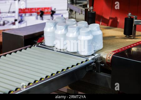 les bouteilles en plastique blanc pharmaceutiques et médicales sont enveloppées dans le film plastique transparent sur la bande transporteuse à la machine d'emballage dans le cosmétique et sup Banque D'Images