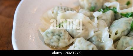 Boulettes fraîches et délicieuses de ciboulette d'ail bouillie aux oignons verts, jiaozi dans une assiette blanche sur fond de table en bois. Banque D'Images