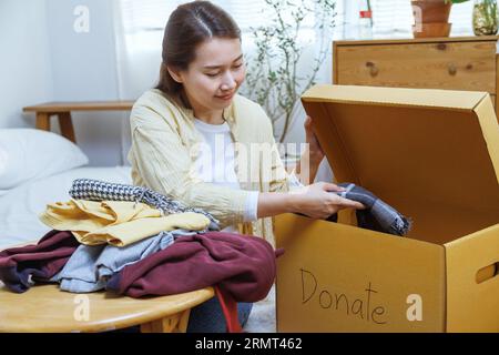 femme asiatique bénévole mettant des vêtements inutilisés dans des boîtes en carton pour don et charité. Réutilisation, recyclage, renouvelable et concept de durabilité. Banque D'Images