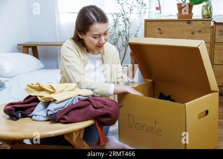 femme asiatique bénévole mettant des vêtements inutilisés dans des boîtes en carton pour don et charité. Réutilisation, recyclage, renouvelable et concept de durabilité. Banque D'Images