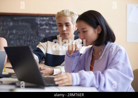 Concentrez-vous sur un jeune homme asiatique confiant faisant une présentation à une camarade de classe féminine assis à côté d'elle et regardant tous les deux l'écran de l'ordinateur portable Banque D'Images