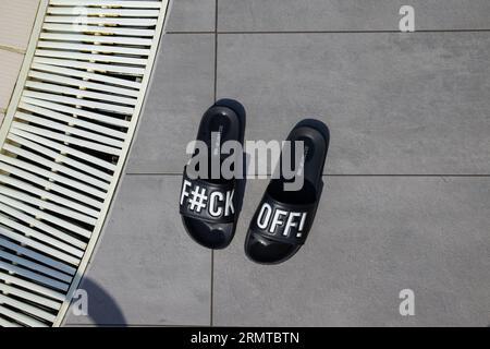 Sandales de piscine avec un message grossier distinctif laissé à côté d'une piscine dans une station de vacances européenne, Simmer 2023 Banque D'Images