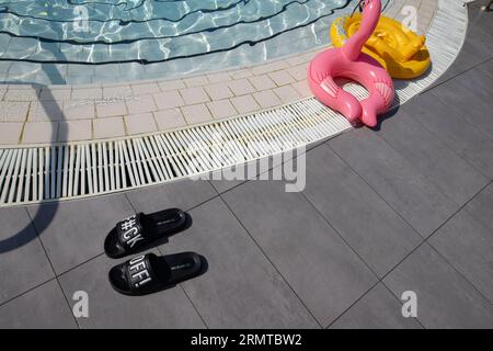 Sandales de piscine avec un message grossier distinctif laissé à côté d'une piscine dans une station de vacances européenne, Simmer 2023 Banque D'Images