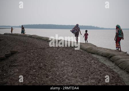 Le 26 août 2023, Khulna, Bangladesh : les gens marchent le long d’une zone boueuse près du barrage endommagé de la rivière après de fortes pluies à Kalabogi dans Khulna. Il n'y a pas si longtemps, Kalabogi, un village côtier du Bangladesh, était plein de terres cultivables jusqu'à ce que la montée du niveau de la mer commence à envahir la région jusqu'au golfe du Bengale. De fréquents cyclones et inondations frappent le village depuis la fin des années 1990 En 2009, un cyclone majeur nommé Aila a détruit les 1 400 kilomètres de remblais du pays, 8 800 kilomètres de routes et environ 3 50 000 acres de terres agricoles. Plusieurs centaines de personnes auraient été tuées à Th Banque D'Images