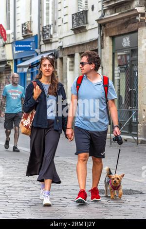 Jeune couple marchant dans le centre-ville main dans la main avec un petit chien terrier - Tours, Indre-et-Loire (37), France. Banque D'Images