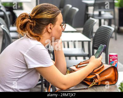 Jeune femme à la table de café en plein air regardant son smartphone - Tours, Indre-et-Loire (37), France. Banque D'Images