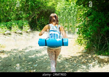 vue du dos d'une femme avec un sac à dos marchant à travers les bois. Banque D'Images