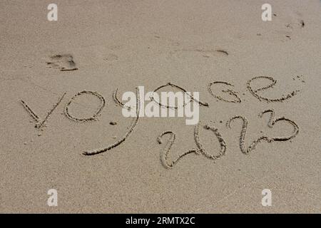 L'inscription voyaje 2022 en français, Voyage 2022, sur le sable par l'eau et la vague montante, mer vacances plage au bord de la mer. Banque D'Images