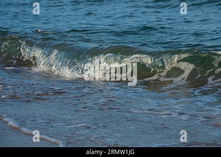 Une grande et forte onde de tempête de couleur turquoise avec des éclaboussures de mousse blanche coule et se brise sur le rivage. Banque D'Images